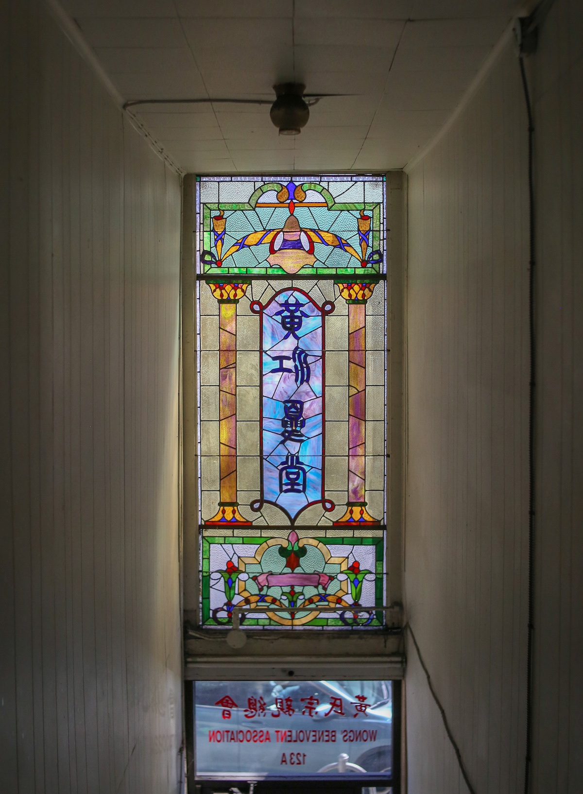 A colourful stained glass window with stylized Chinese characters in the centre, seen from the inside of a building.