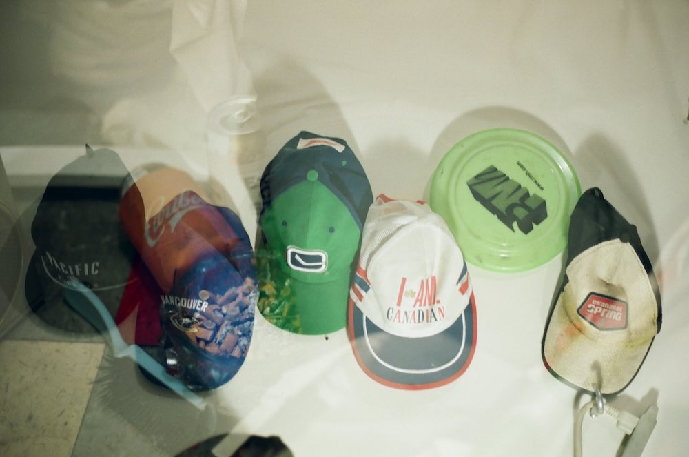 A double-exposure image depicts a row of ball caps arranged horizontally against a white wall with various logos on them, plus, on the right, a neon green plastic Frisbee.