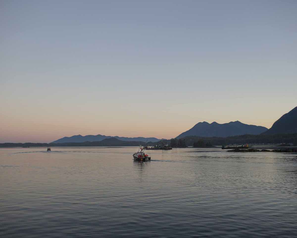 A fishing boat leaves the Tofino harbour at dusk. The darkening sky is pink and blue.