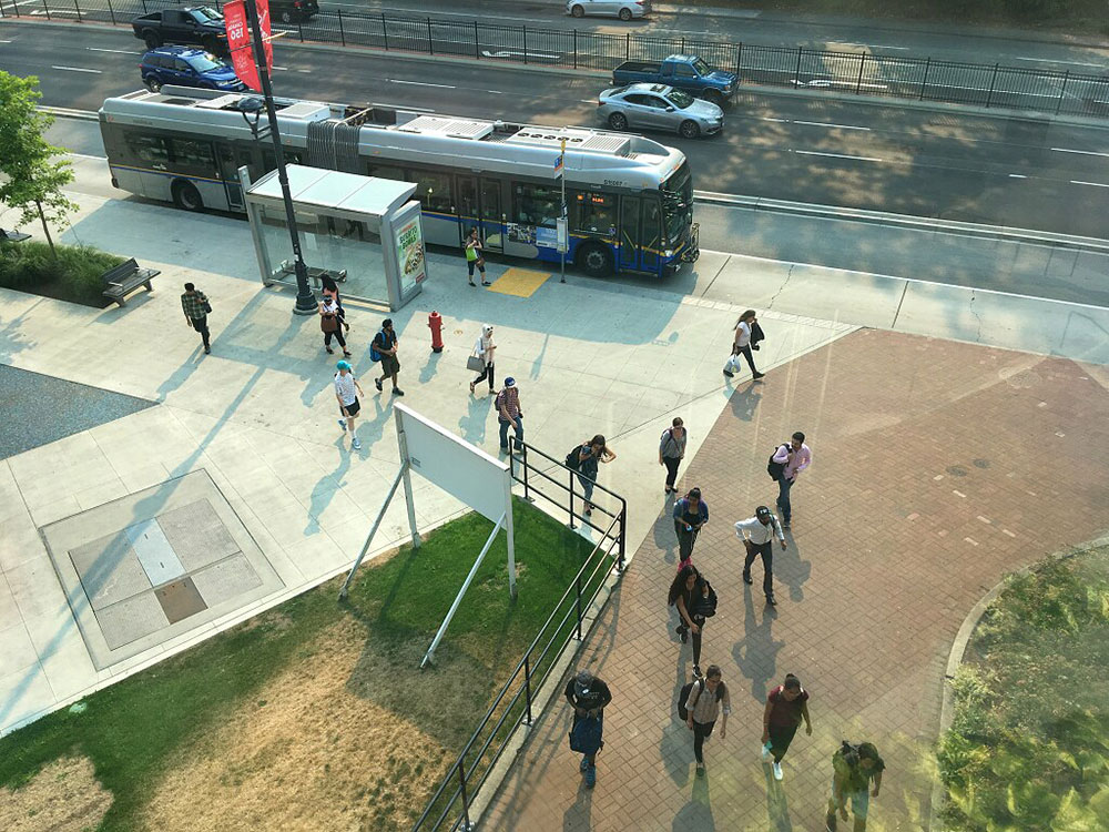 Aerial view of about a dozen people walking away from a public bus at a bus stop.