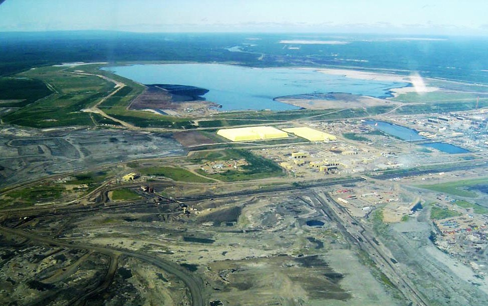 An aerial photo shows vast areas stripped of ground and a large tailings pond.