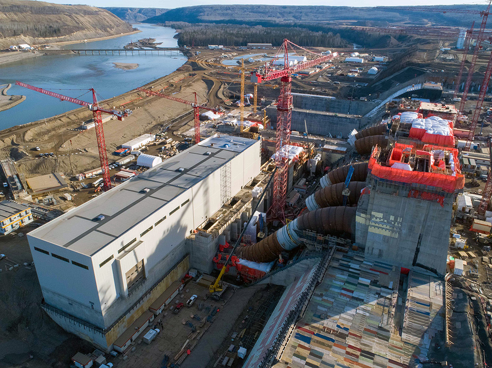 An aerial photo of a massive dam construction site. The foreground shows a generating station with several large tube-like passages.