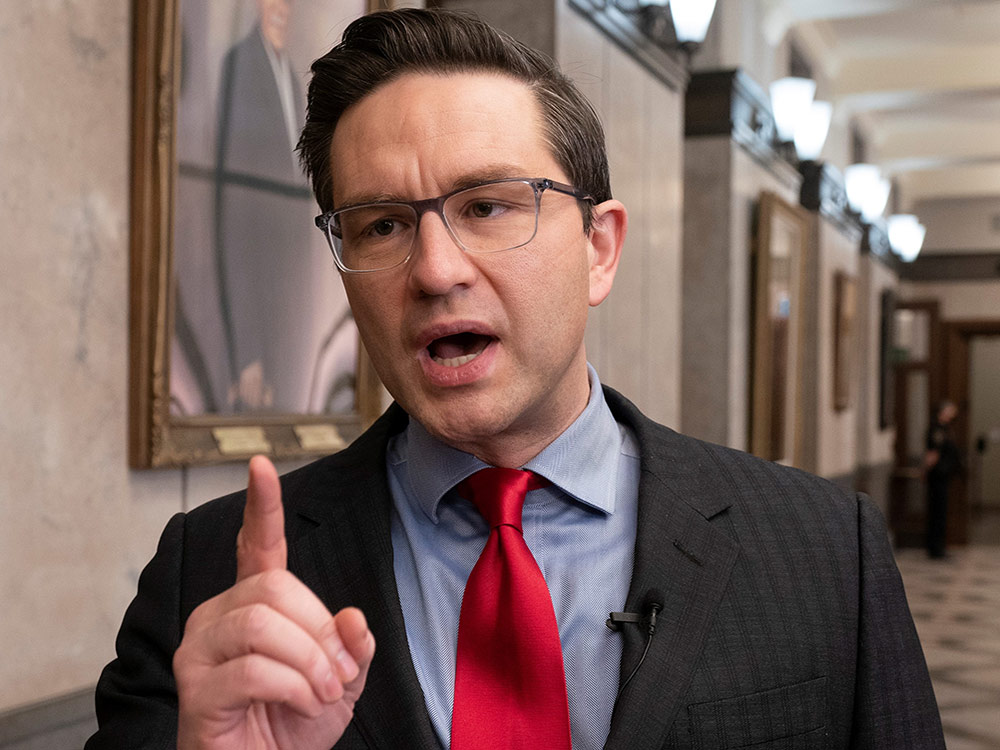 Pierre Poilievre, in a dark suit with thick combed black hair and wire framed glasses, wags his finger while talking.