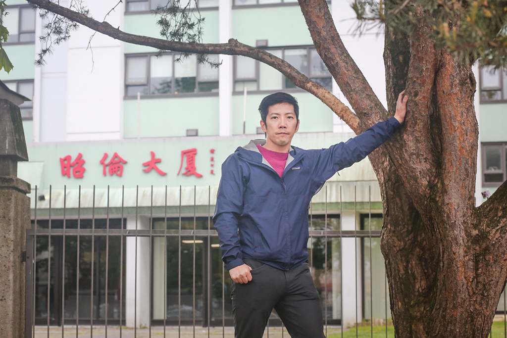 Mike Tan, the vice-president of the Chau Luen Society, leans against a tree. Behind him is his society&rsquo;s tower for seniors. The tower is painted lime green, and at the entrance are the traditional Chinese characters for Chau Luen Society in red.