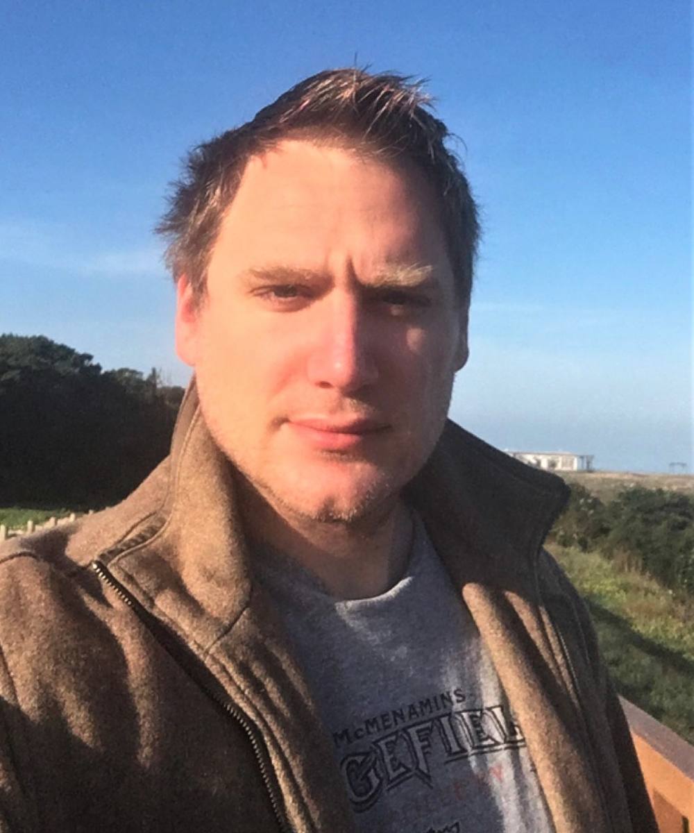 A picture of Anthony Leonardi, outdoors and wearing a brown coat.