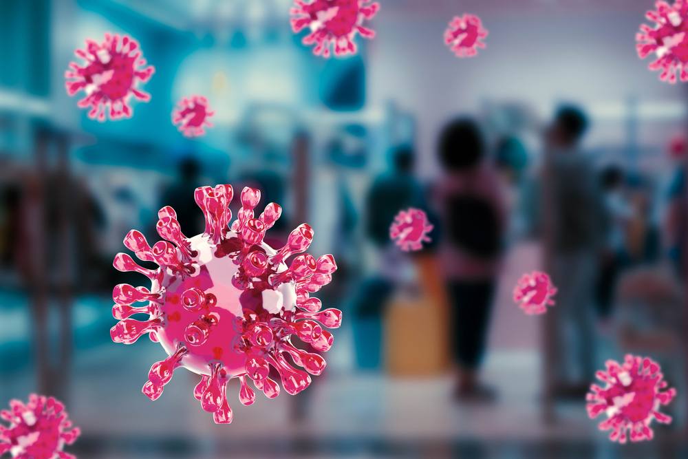 A photo montage shows images of the coronavirus blown up large with people in a building out of focus in the background.