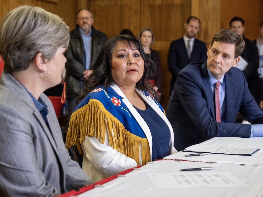 Three people sit at a long table angled towards the camera. B.C. Energy Minister Josie Osborne is in the foreground, Chief Judy Desiarlais is centre, and Premier David Eby is furthest back.