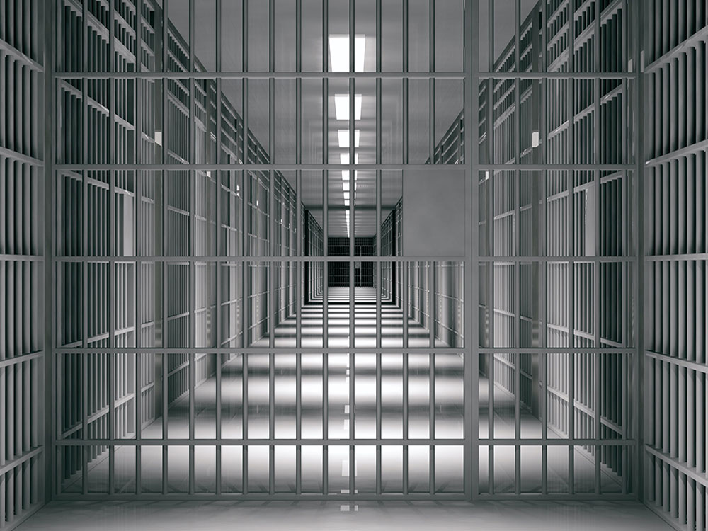 A long corridor with jail cells on each side stretching into the distance.
