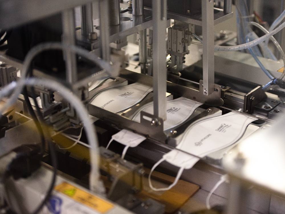 A stainless steel assembly line produces a flat assortment of white CAN99 masks. 