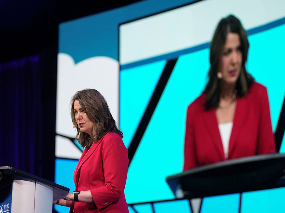 Danielle Smith gives a speech wearing a red blazer.