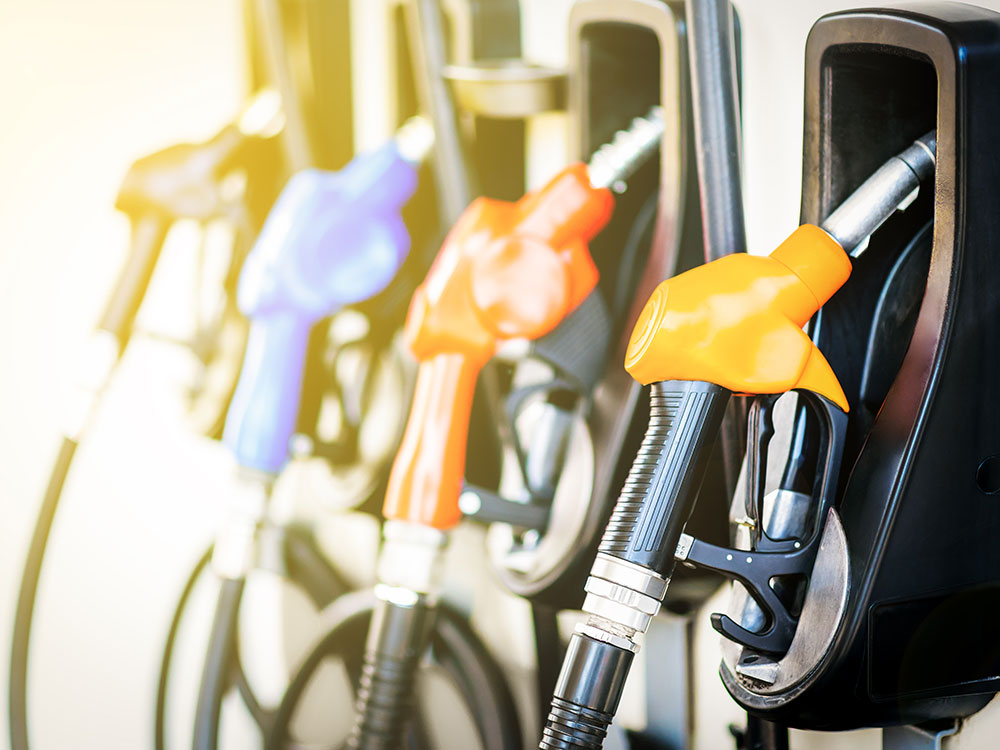 A row of colourful pump nozzles at a gas station are illuminated in warm sunset light.