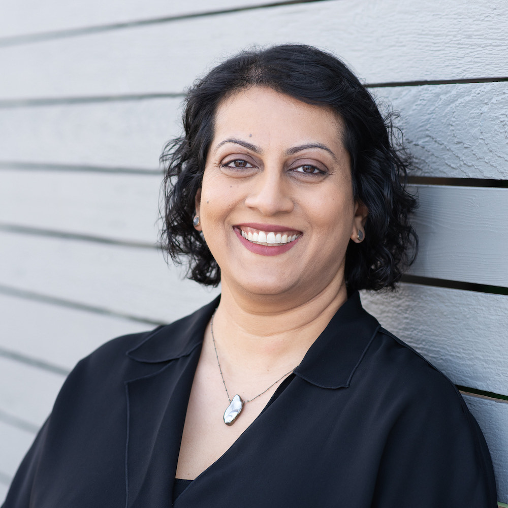 A woman with medium skin tone and a dark, curly bob smiles at the camera.