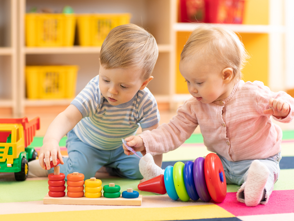 Two babies play with colourful stacking doughnuts.