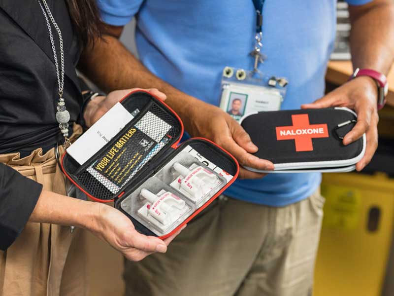 A close-up photo of an open nasal Naloxone kit, left, and a closed Naloxone kit, right.