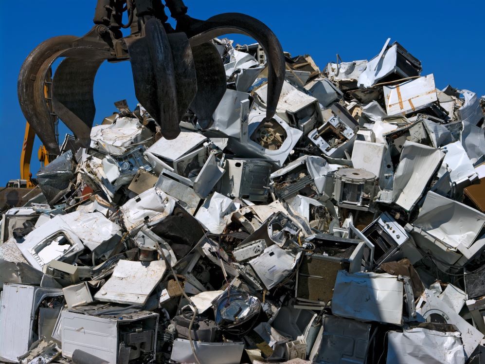 A large metal claw descends upon a scrap heap of discarded appliances and other metal objects.
