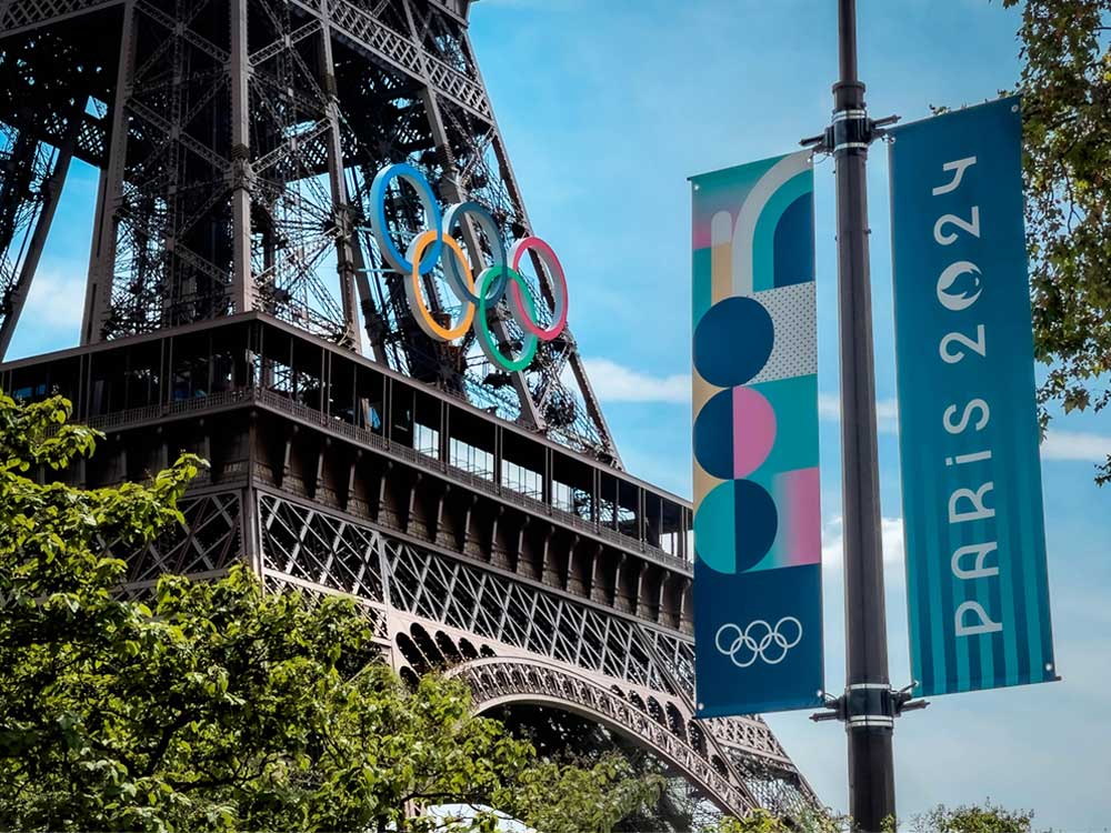Olympic rings have been installed onto the Eiffel Tower. Banners attached to a nearby lamppost read, ‘Paris 2024.’