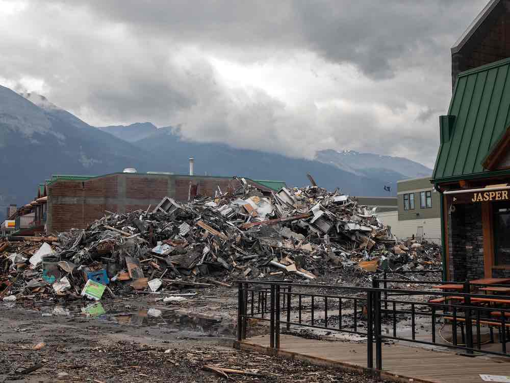 A pile of rubble sits on a lot, while nearby structures appear untouched.