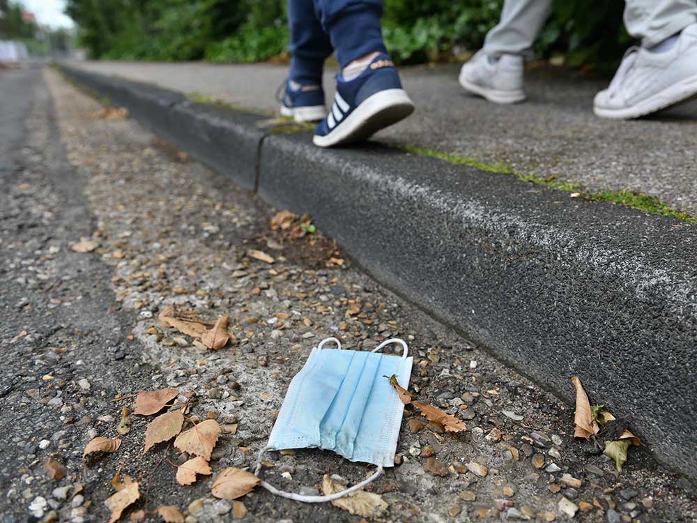 A surgical mask is abandoned in a gutter as people walk past.