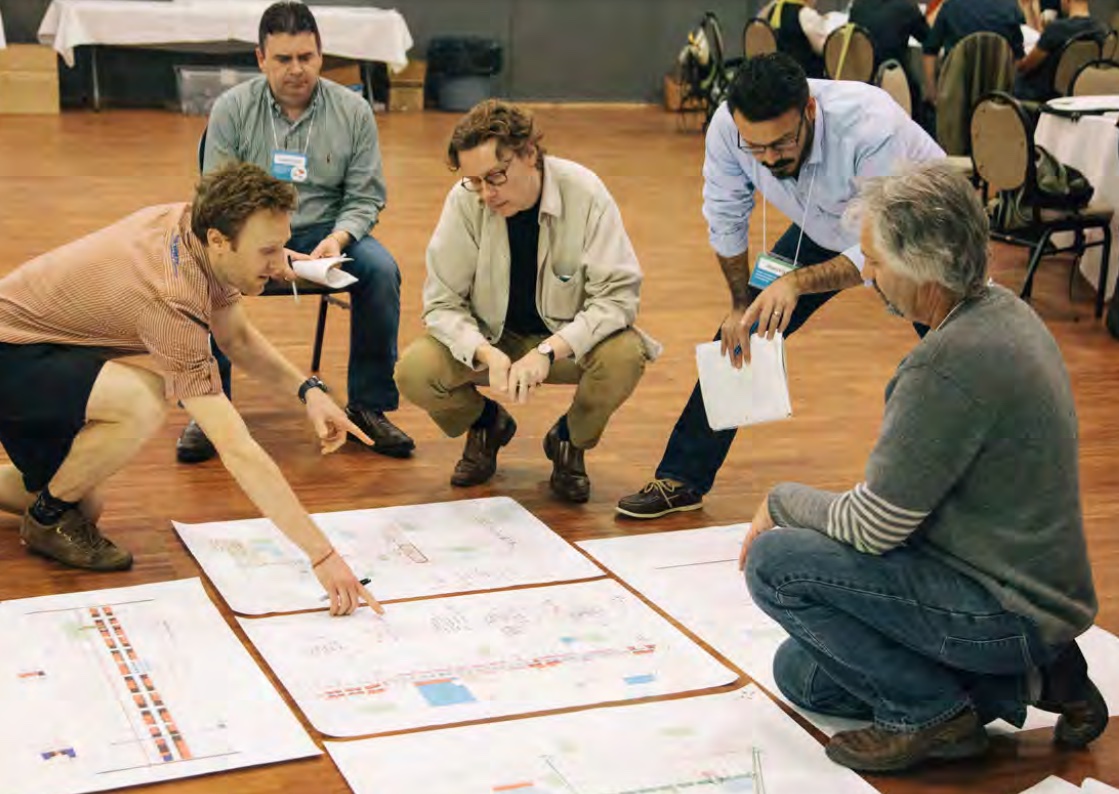 Five people crouch around a series of diagrams spread out on the floor.