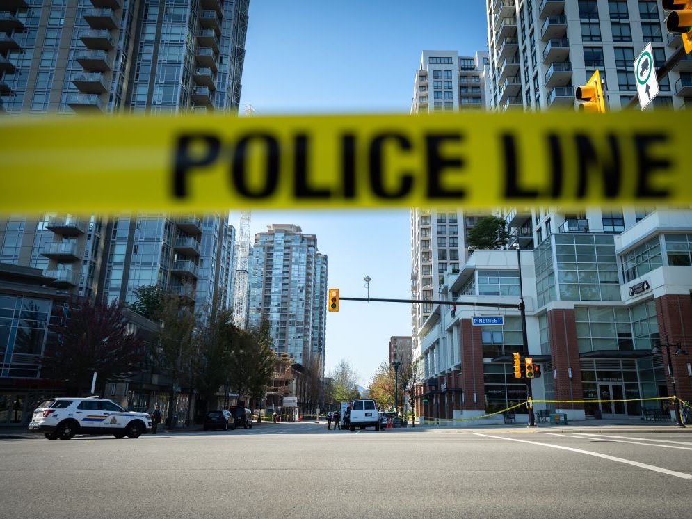 A strip of yellow and black police tape stretches across a road with highrises in the background.