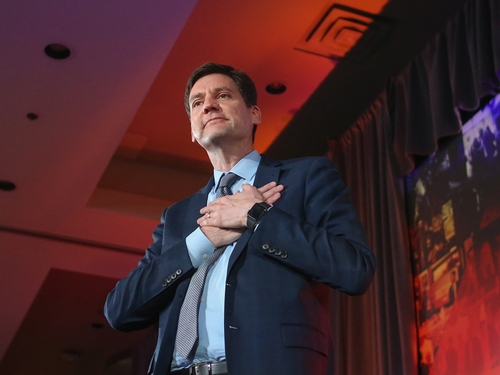 David Eby stands onstage on election night, his hands over his heart expressing gratitude.