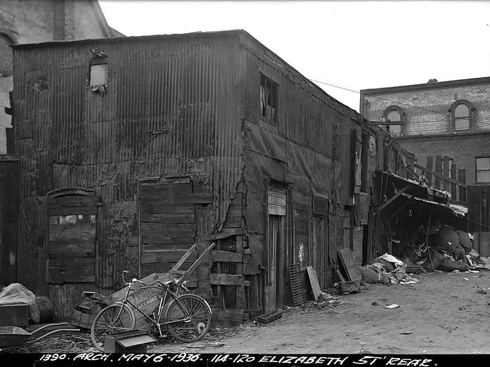 A black and white photo showing a wood-framed building cladded in corrugated metal.