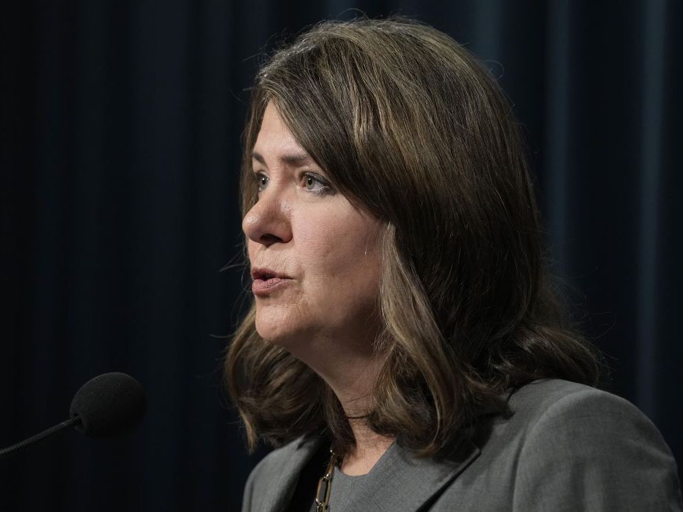 A middle-aged white woman with shoulder-length brown hair is shown in profile, speaking.