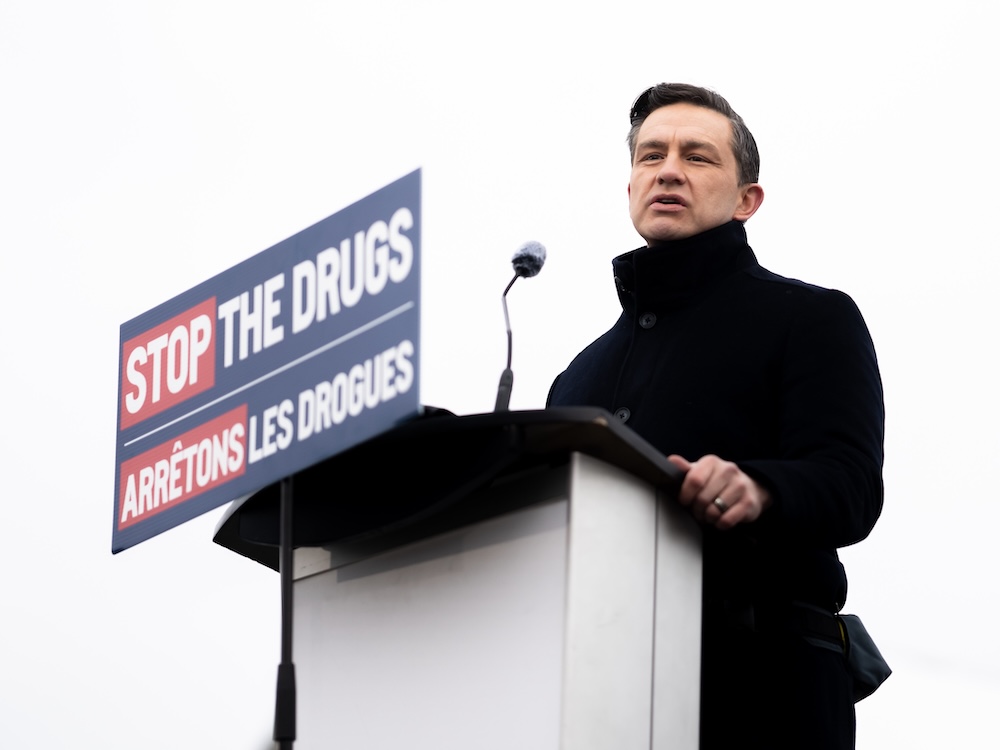 Pierre Poilievre stands at a podium with a sign that reads, 'Stop the Drugs, Arrêtons les drogues.'