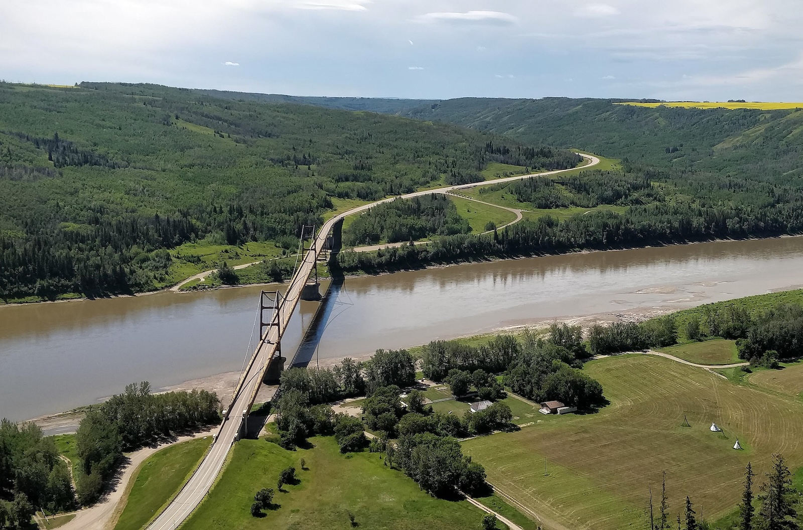 Aerial view of a bridge over a wide brown river in a green landscape.