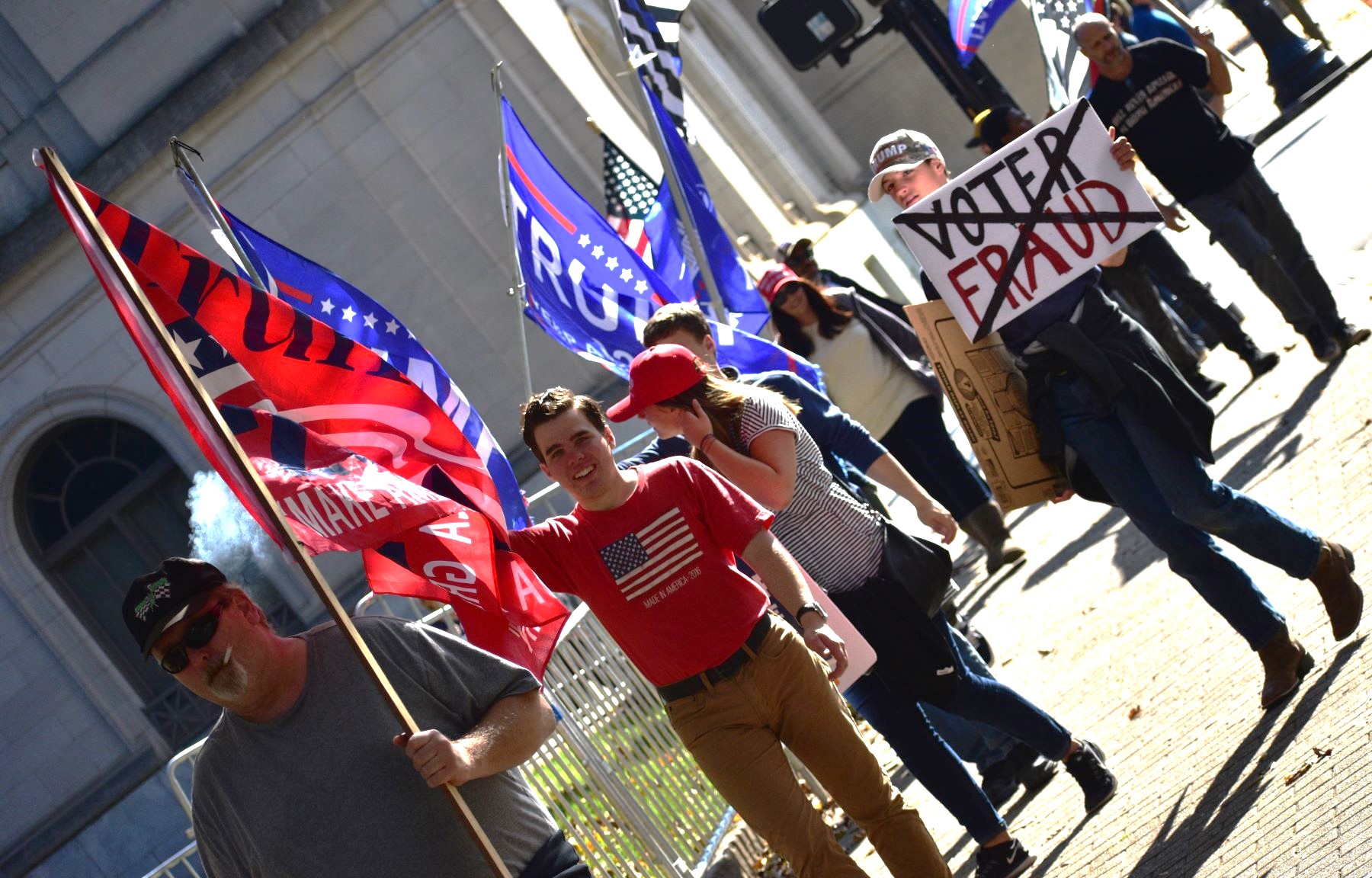 A diagonally shot photo captures protesters walking in a group, holding Trump and U.S. flags, as well as wearing Trump hats and U.S.-flag hats and t-shirts.
