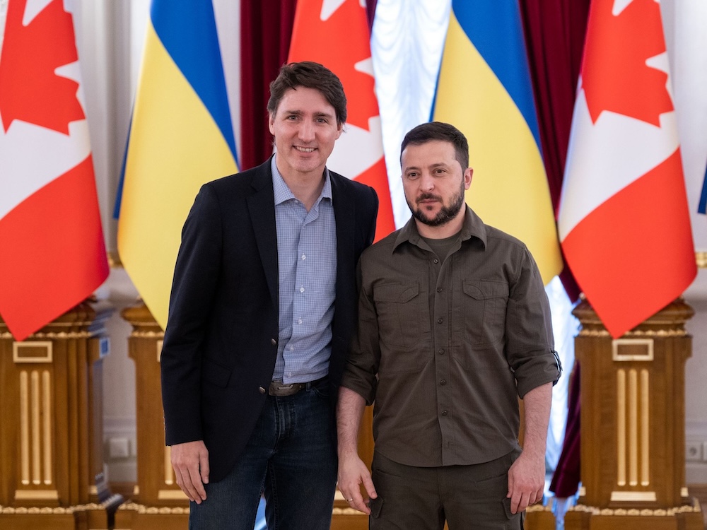 Justin Trudeau stands to the left of Volodymyr Zelensky in front of a row of alternating Canadian and Ukrainian flags.