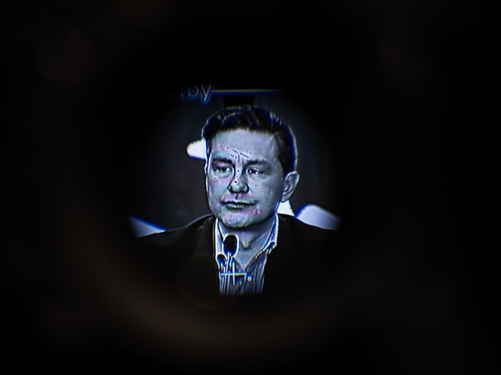 Pierre Poilievre appears on a screen inside a screen. He is monotone, in black and white and blue. 