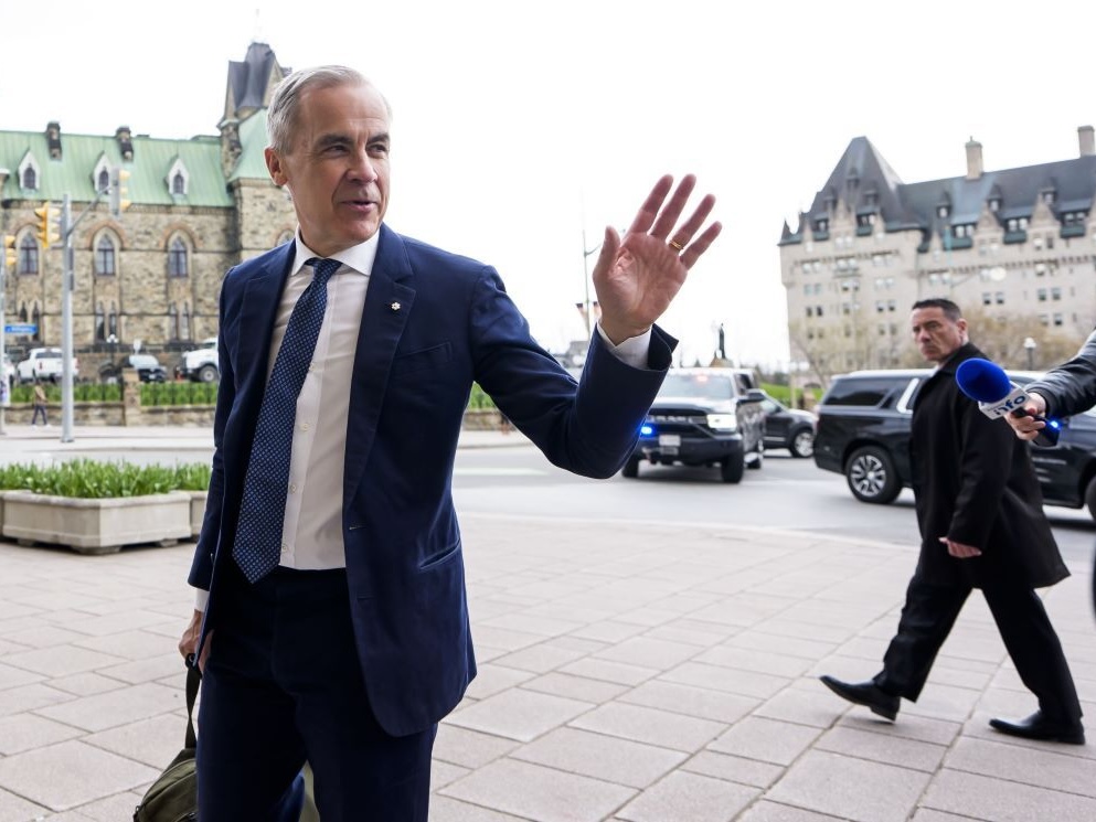 Mark Carney, a slim 60-year-old man in a suit, waves outside the Parliament Buildings in Ottawa.