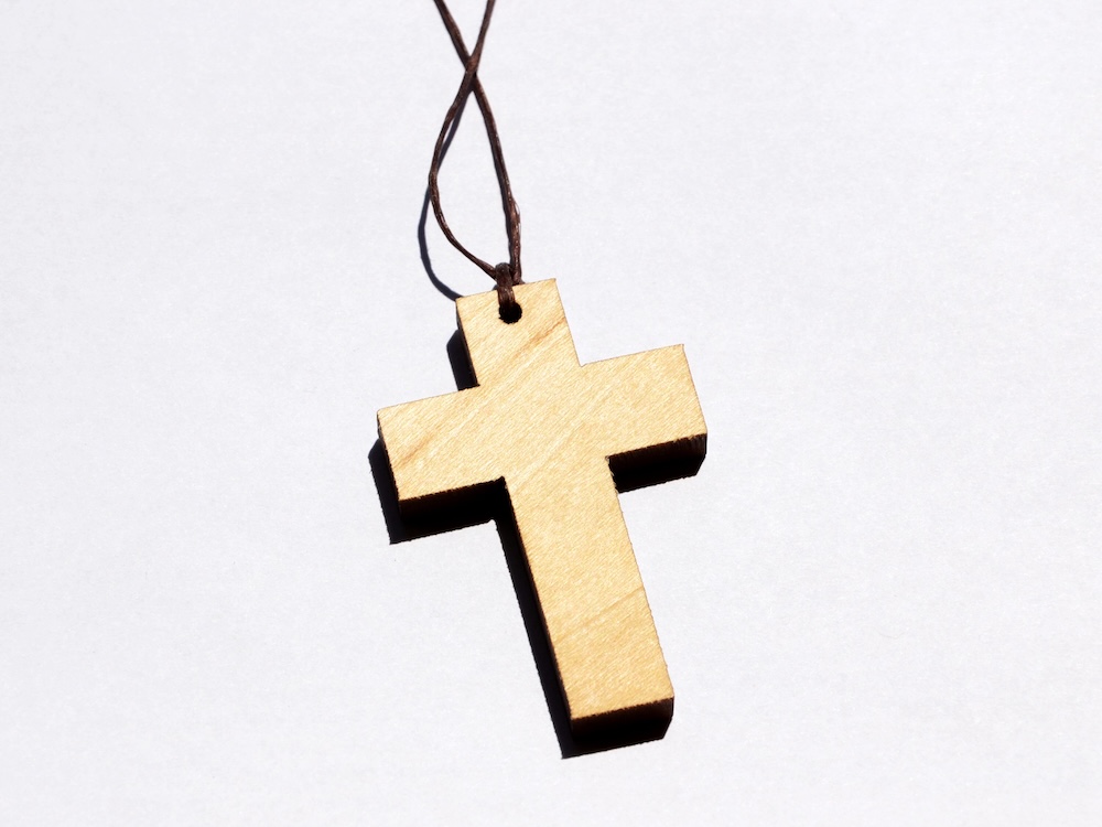 A wooden cross pendant is tied at its top end with a brown piece of twine against a white background.