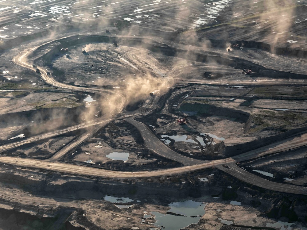 An aerial photo shows blackened ground and dust trails from giant trucks criss-crossing an oilsands mine site.