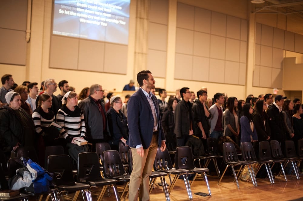 A 40-ish light-skinned man stands in the front row of several dozen church members.