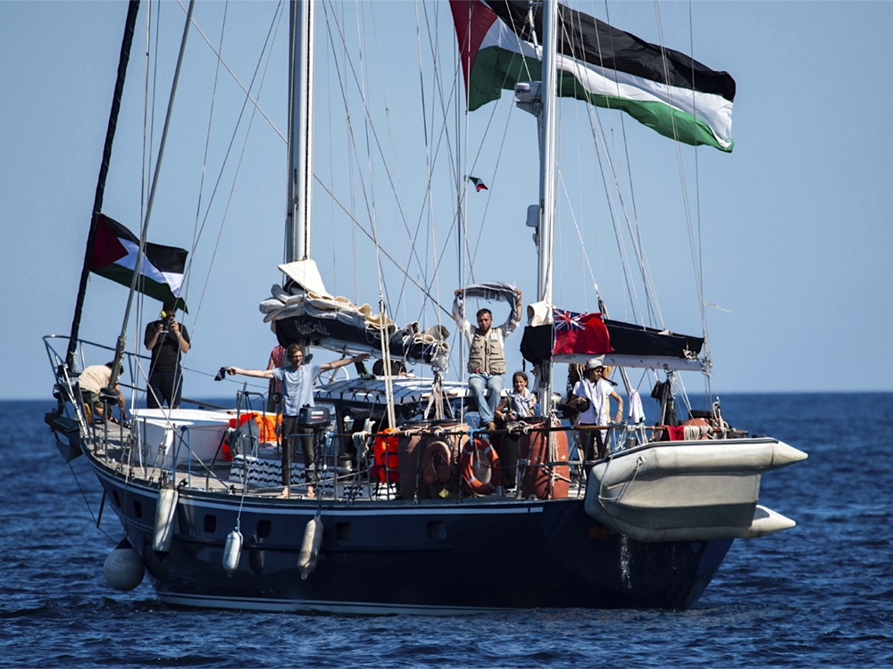 About a half-dozen people are visible on a sailboat adorned with Palestinian flags. 