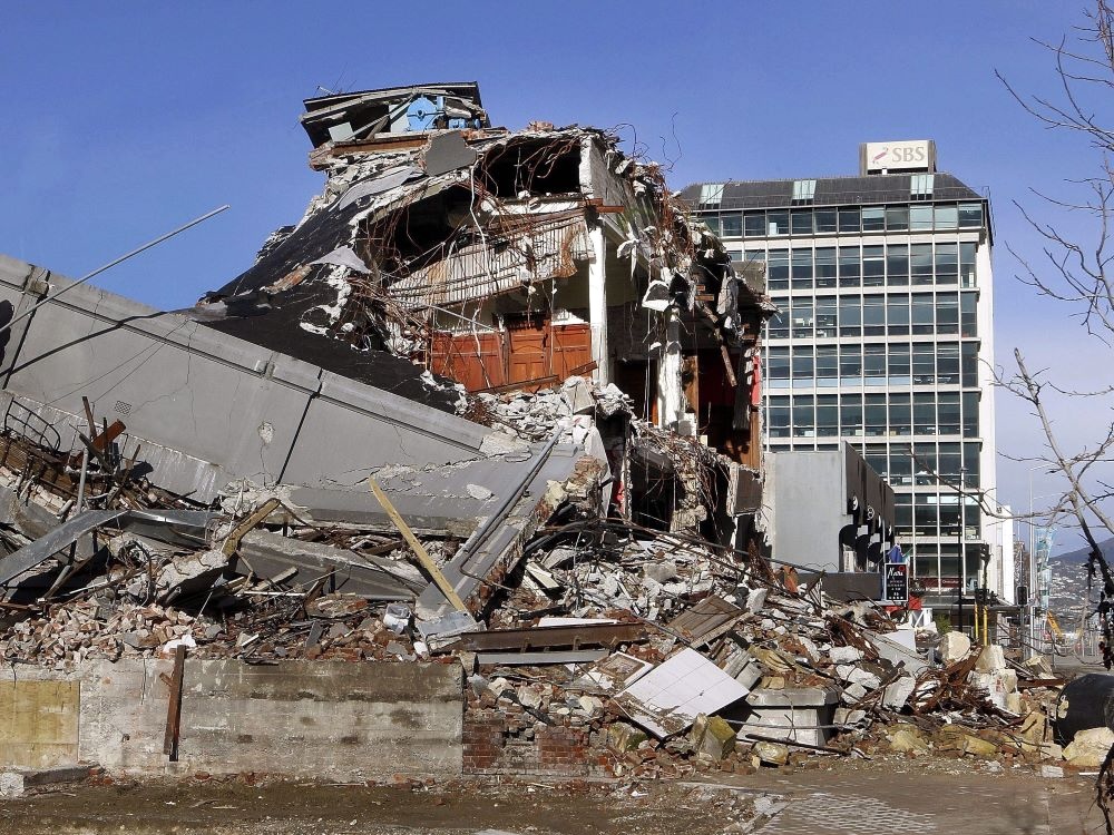 A building in ruins surrounded by rubble, with an intact building behind it.