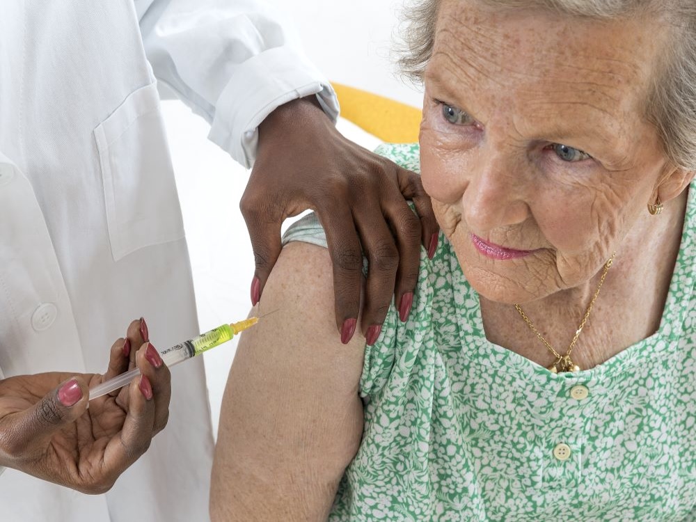 An elderly woman receives a vaccination in the arm.