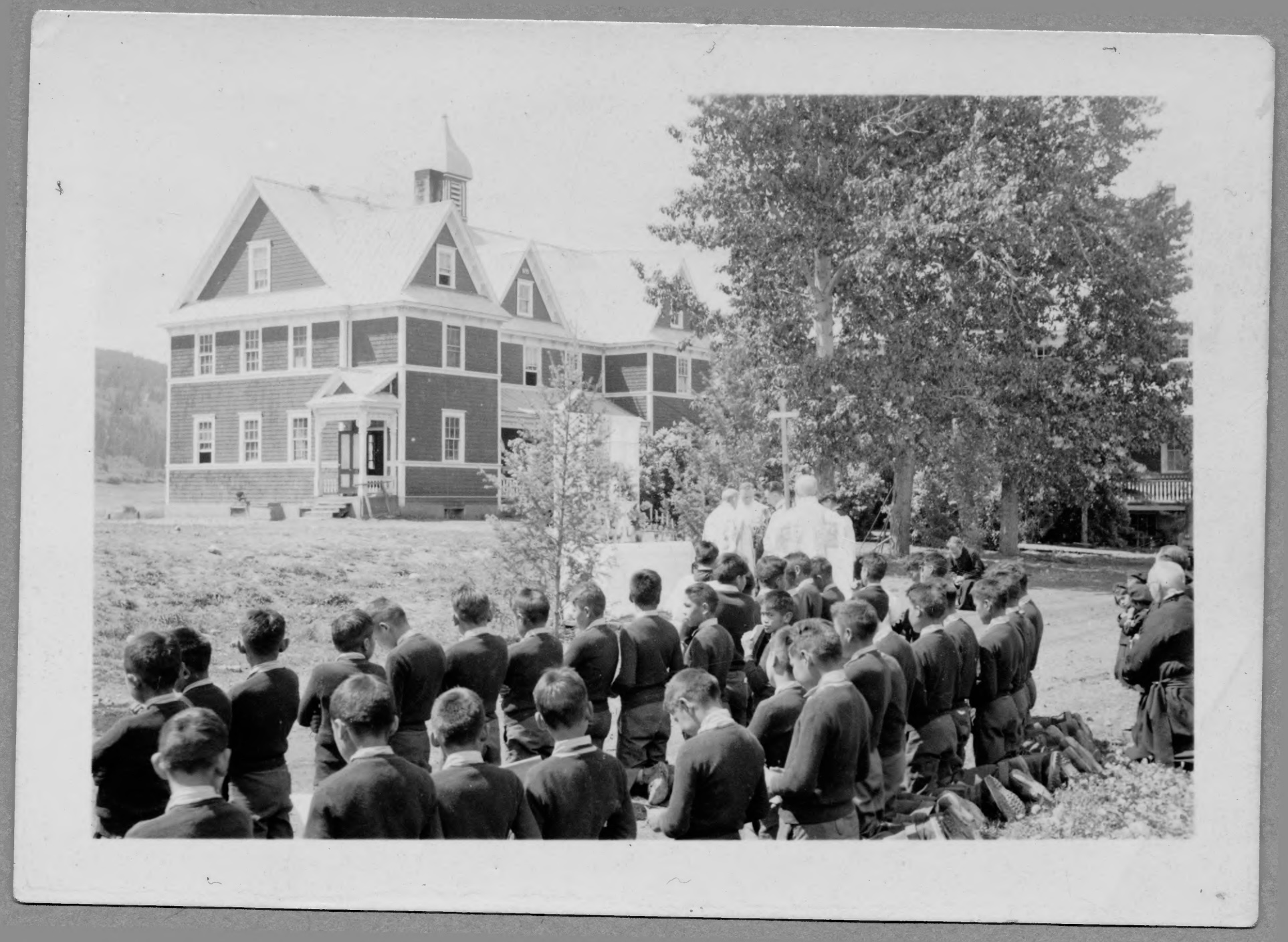 A black and white photo of a residential school in British Columbia, with a group of students in the foreground.