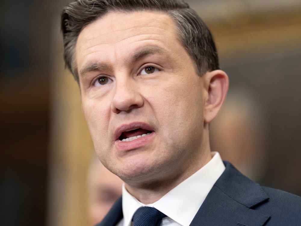 Close-up of Pierre Poilievre, a light-skinned man with short dark hair wearing a navy blue suit and tie, in mid-speech.