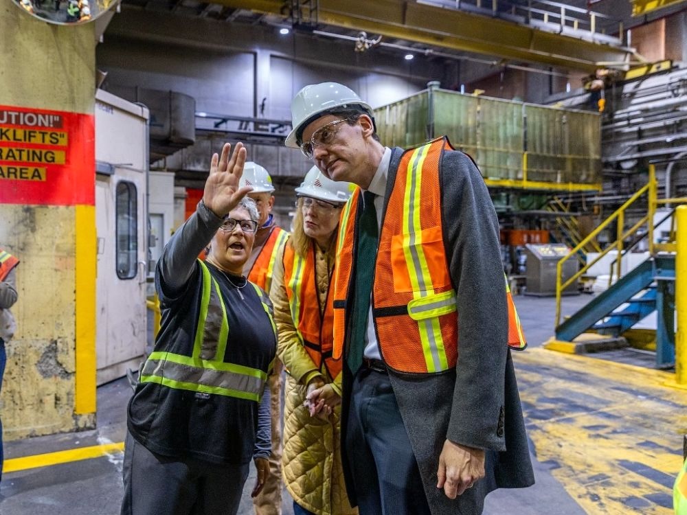 A very tall fair-skinned man wearing a high-vis vest cranes his neck to listen to a fair-skinned woman say something.