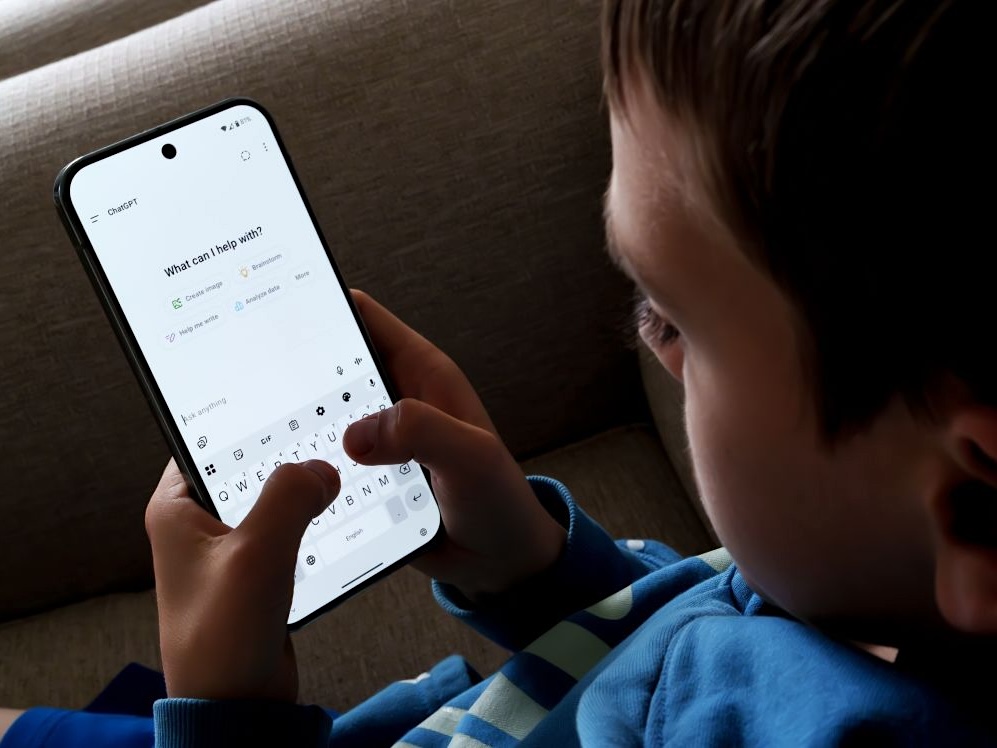 A boy holds a phone that displays a ChatGPT screen.