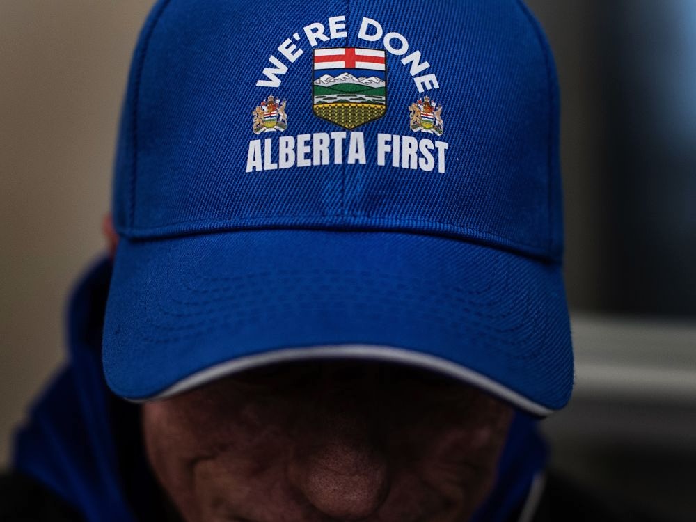 A man wears a blue hat with Alberta provincial emblems and the words &lsquo;We&rsquo;re Done. Alberta First.&rsquo;