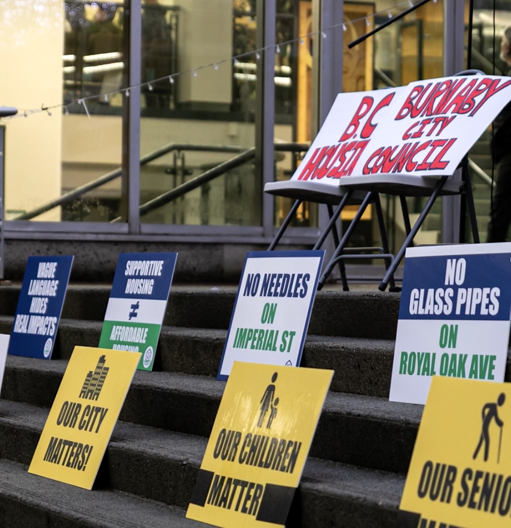 Protest signs are arranged on concrete steps. They read &lsquo;Our children matter,&rsquo; &lsquo;No glass pipes on Royal Oak Ave.,&rsquo; &lsquo;No needles on Imperial St.,&rsquo; &lsquo;Supportive housing does not equal affordable housing&rsquo; and &lsquo;Vague language hides real impacts.&rsquo;