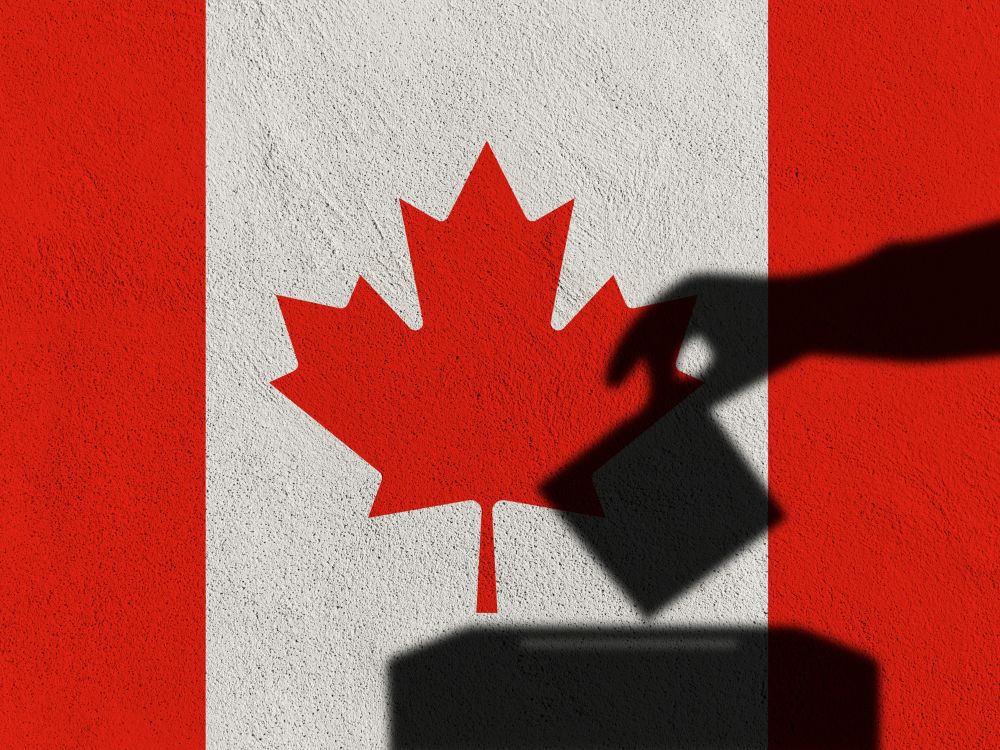 A shadow of a hand placing a ballot in a box with the Canadian flag behind.