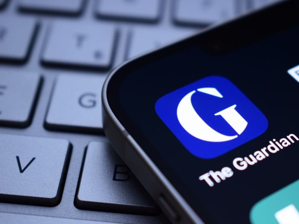 A smartphone lays upon a keyboard. On its screen is a white &ldquo;G&rdquo; against a blue background, symbolizing the Guardian newspaper.