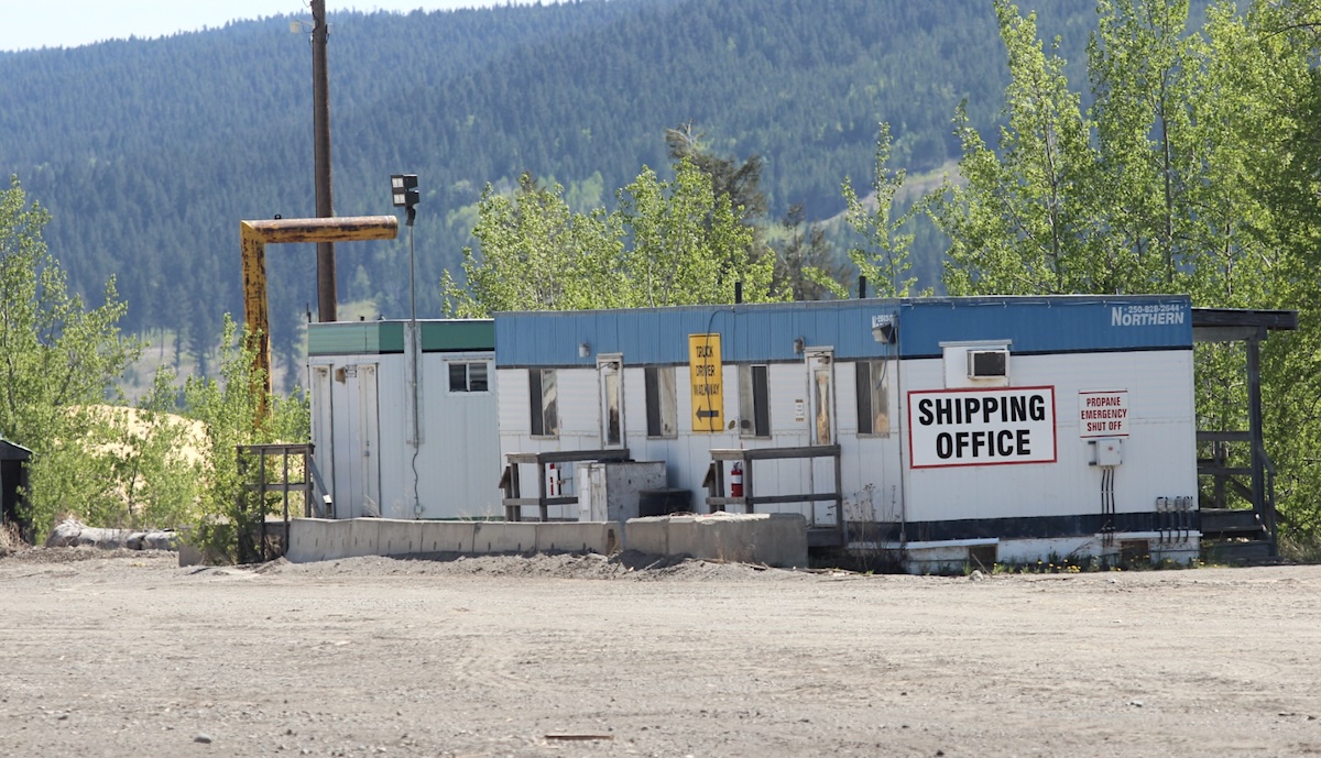 A squat modular with a &lsquo;Shipping Office&rsquo; sign sits on a large, empty lot. 