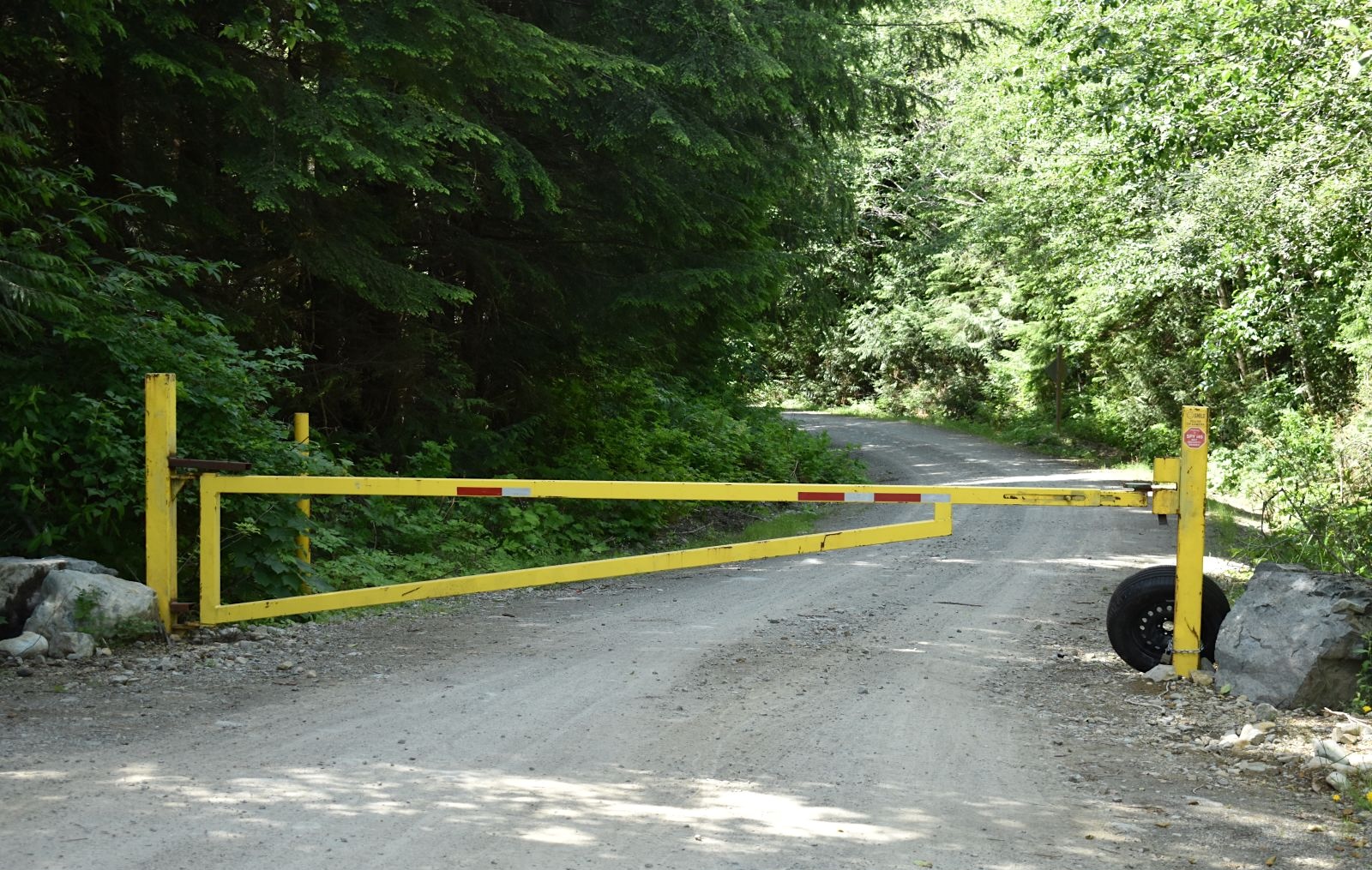 A yellow gate blocks a gravel road in a forested area.