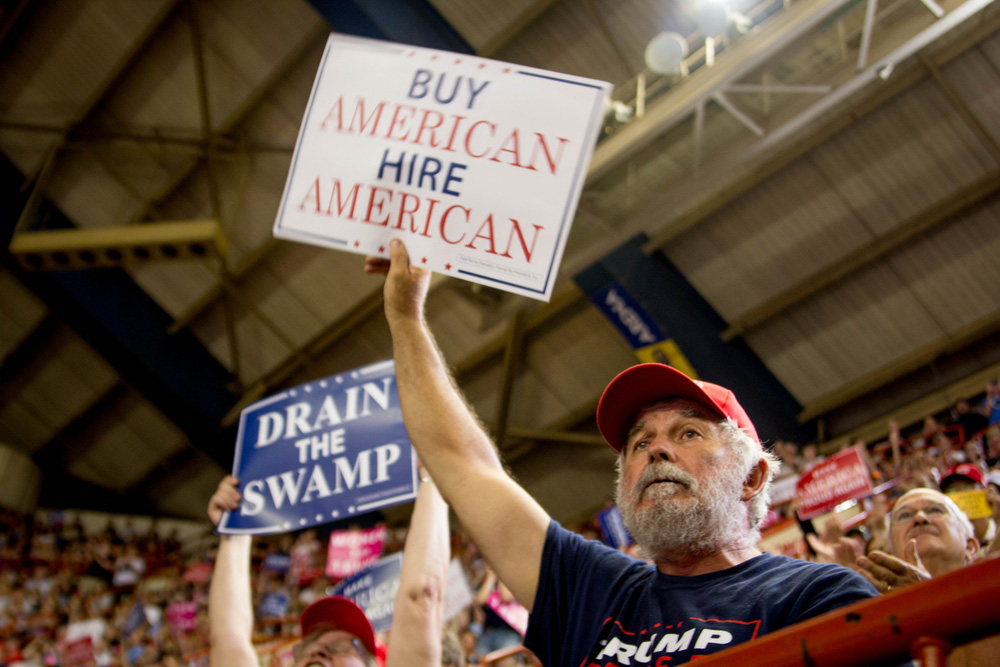 People at a Trump rally hold up signs reading things like 'Buy American, Hire American' and 'Drain the Swamp.'